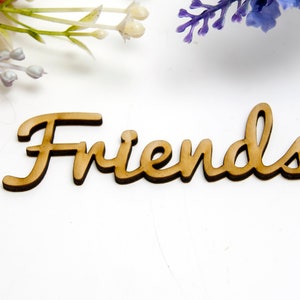 Könnte beinhalten: Ein Holzschild mit dem Wort "Friends" in kursivschrift. Das Schild ist hellbraun und hat einen leicht abgenutzten Look.