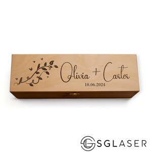 Puede incluir: Una caja de madera grabada con un diseño de una vid con pájaros y hojas. La caja está personalizada con los nombres "Olivia + Carter" y la fecha "10.06.2024".