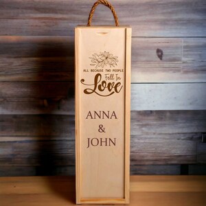 Könnte beinhalten: Eine Weinkiste aus hellem Holz mit einem Seilgriff. Auf der Kiste stehen die Worte "ALL BECAUSE TWO PEOPLE Fell In Love" und die Namen "ANNA & JOHN".