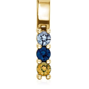 May include: A gold pendant with three gemstones. The top gemstone is light blue, the middle gemstone is dark blue, and the bottom gemstone is yellow.