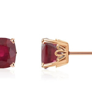 May include: A pair of rose gold earrings with a square-shaped ruby gemstone in each earring.