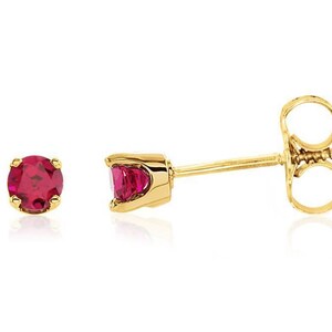 May include: A pair of gold stud earrings with a red gemstone in each. The earrings have a screw-back closure.