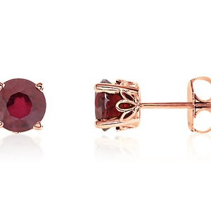 May include: A pair of rose gold stud earrings with a round, red gemstone in each earring.