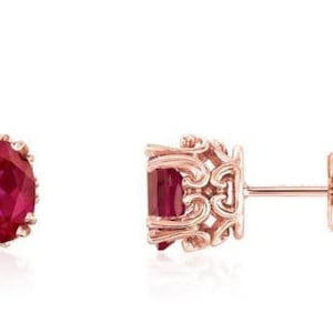 May include: A pair of rose gold earrings with oval-shaped ruby gemstones set in a delicate filigree design.
