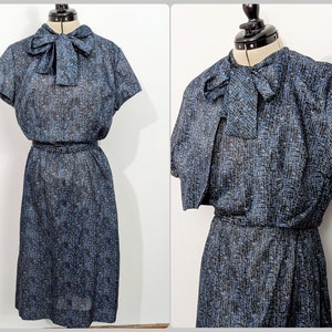 May include: A blue and black patterned dress with a matching jacket. The dress has a bow at the neckline and a belt at the waist. The jacket has a short, cropped style.