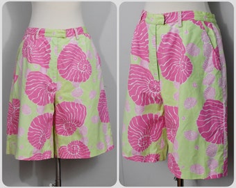 May include: A pair of green and pink shorts with a seashell pattern. The shorts have a button and zipper closure and two pockets.