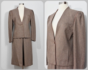 May include: A brown wool skirt suit with a V-neck jacket and a skirt that hits below the knee. The jacket has a single button closure and a brown trim around the edges.