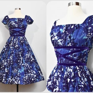 May include: A vintage blue and white patterned dress with a purple velvet sash. The dress has a square neckline and short sleeves.