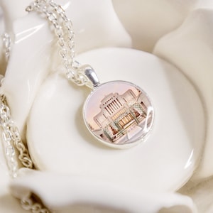 May include: A silver chain necklace with a round pendant featuring a photograph of a white building with a pink sky in the background.