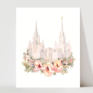 May include: Watercolor print of a white building with two spires, topped with a gold accent. The building is surrounded by a wreath of pink and peach flowers and green foliage, set against a white background.