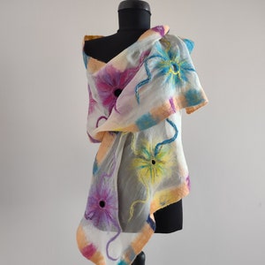 Puede incluir: Una bufanda de seda blanca con un diseño floral en tonos de rosa, amarillo, azul y verde. La bufanda está drapeada sobre un maniquí negro.