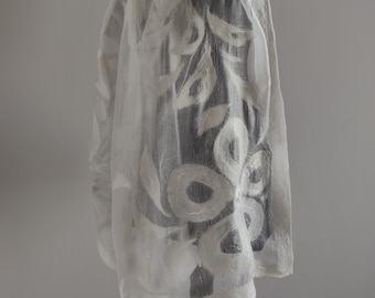Puede incluir: Una bufanda blanca de gasa con un delicado diseño floral blanco. La bufanda está drapeada sobre un maniquí negro.