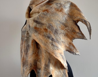 May include: A felted wool scarf in shades of tan, brown, and gray, draped over a black mannequin. The scarf has a textured appearance with a unique, pointed edge design. The scarf is a wearable art piece.