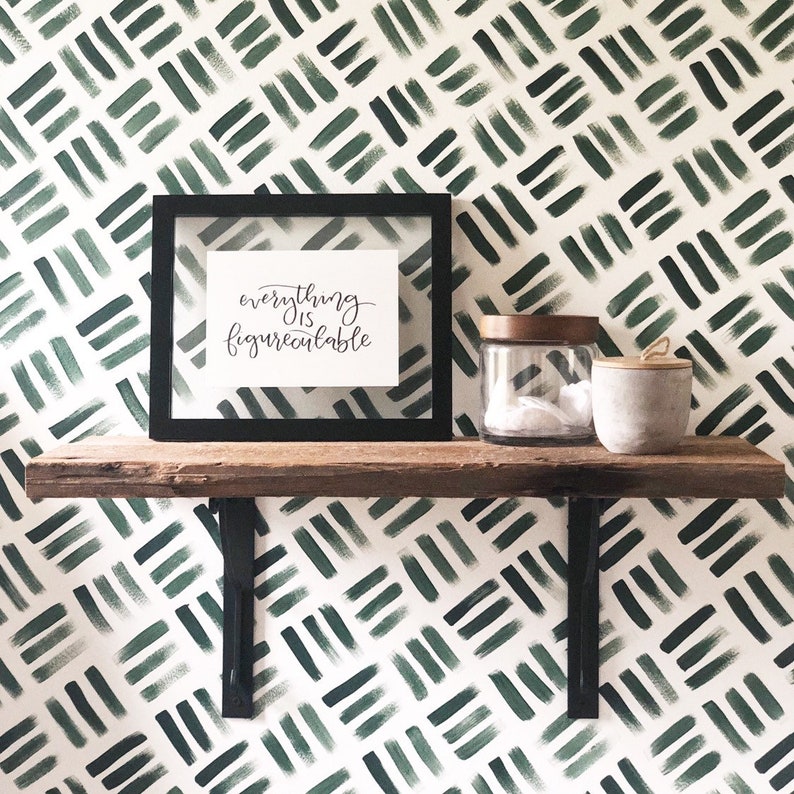 K&ouml;nnte beinhalten: Ein Holzregal mit schwarzen Metallkonsolen ist an einer wei&szlig;en Wand mit einer gr&uuml;n-wei&szlig;en geometrischen Mustertapete montiert. Ein gerahmter Druck mit dem Text "everything is figureoutable" befindet sich auf dem Regal. Auf dem Regal stehen zwei Glasbeh&auml;lter mit Deckeln.