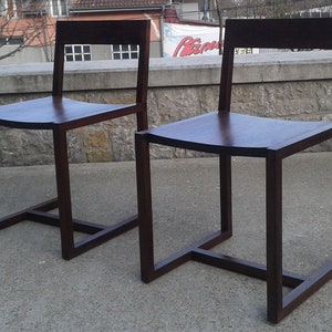 May include: Two dark brown wooden chairs with a square frame and a curved seat.