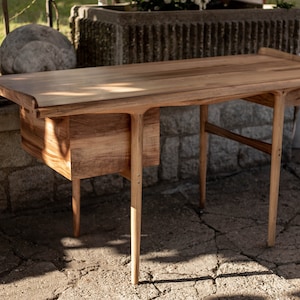 May include: A wooden desk with a natural finish and two drawers. The desk has a unique design with curved edges and legs.