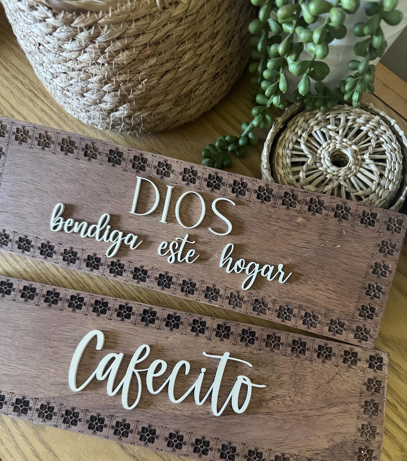 Puede incluir: Dos placas de madera con letras blancas y un borde floral. La placa superior dice "DIOS bendiga este hogar" y la inferior "Cafecito". Las placas son de color marr&oacute;n c&aacute;lido.