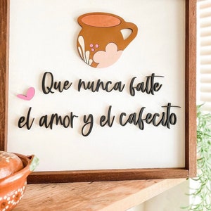 May include: A wooden sign with a brown and pink coffee cup cutout and the text "Que nunca falte el amor y el cafecito" in black lettering.