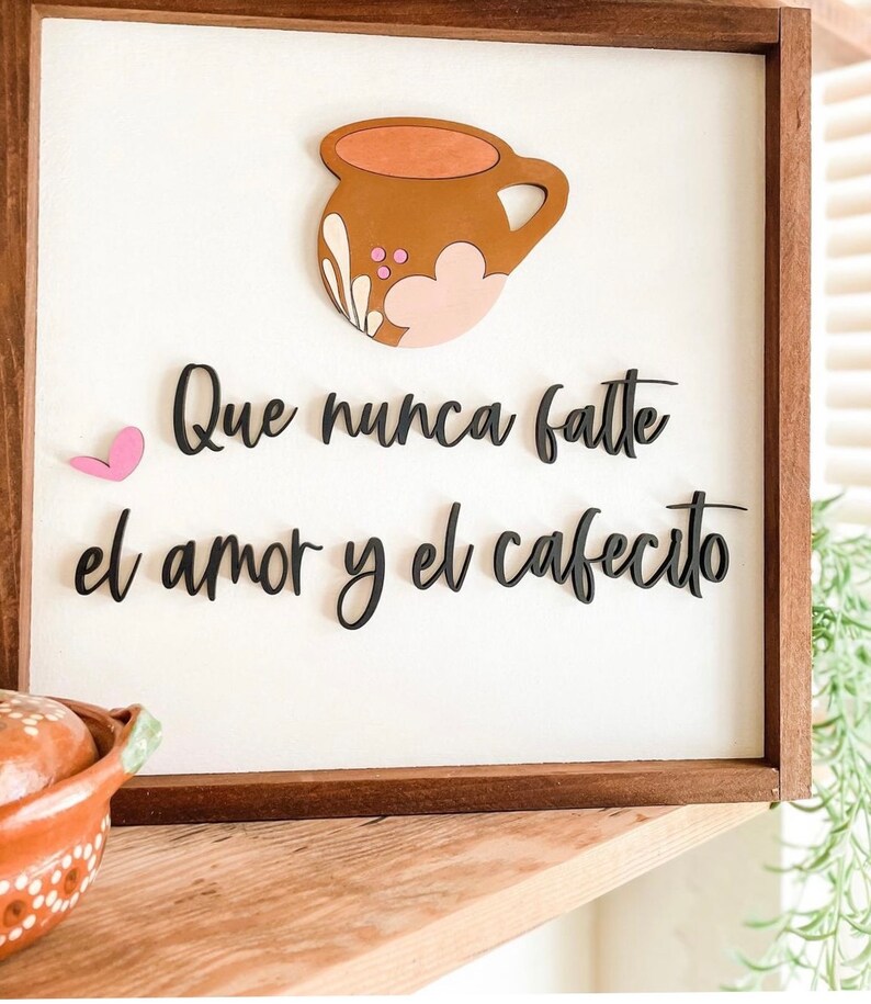 May include: A wooden sign with a brown and pink coffee cup cutout and the text "Que nunca falte el amor y el cafecito" in black lettering.