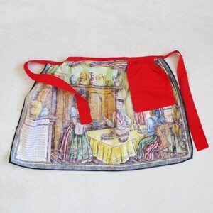 Puede incluir: Un delantal de cocina rojo y blanco con una ilustraci&oacute;n vintage de personas reunidas alrededor de una mesa. El delantal tiene un bolsillo rojo en la parte delantera y cintas rojas.