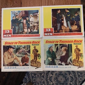 Peut inclure: Quatre cartes de lobby de film vintage présentant des scènes de 13 Fighting Men et Stage to Thunder Rock. Chaque carte rectangulaire affiche des images de film colorées, des titres en gras et des noms d'acteurs imprimés en blanc et rouge.