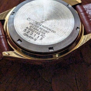 Pu&ograve; includere: Primo piano del retro di un orologio Citizen color oro con cinturino in pelle marrone. Il retro dell'orologio &egrave; in acciaio inossidabile e presenta il testo "CITIZEN WATCH CO. WATER RESIST STAINLESS 4-R02149 AC 523115 GN-4W-S".