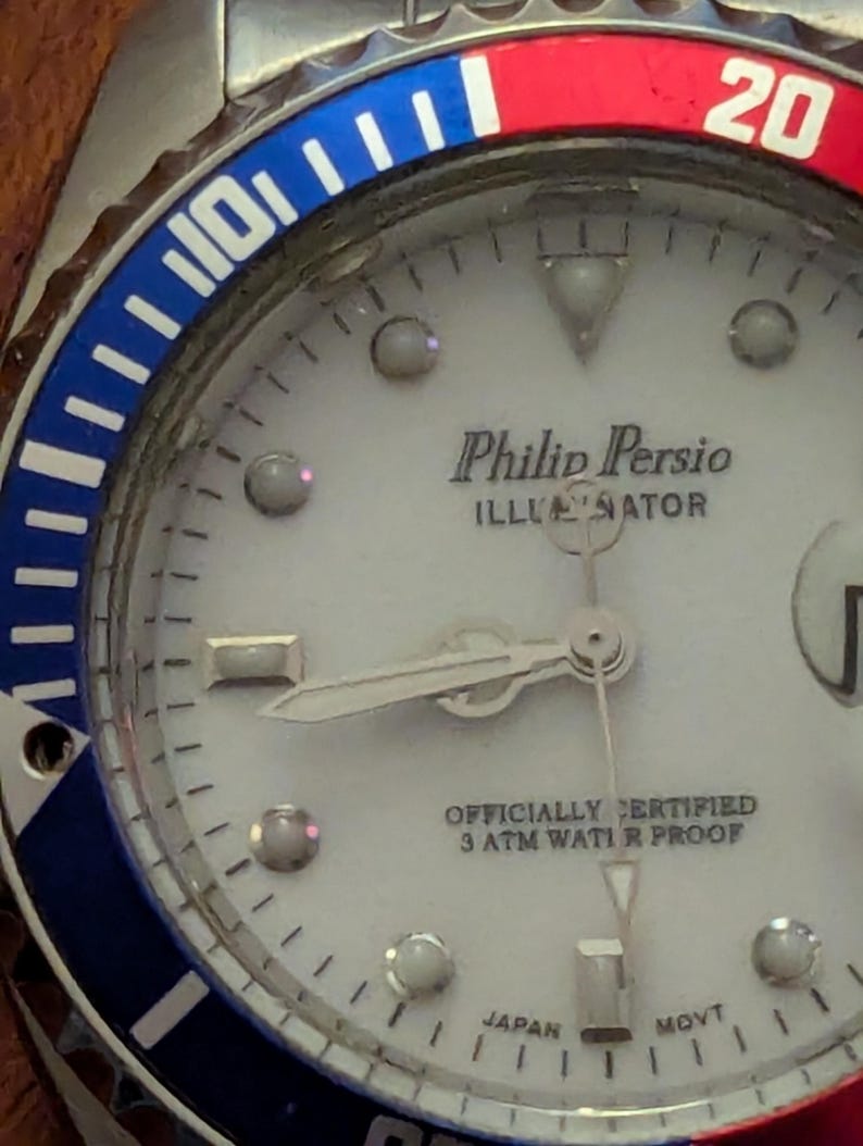 May include: A Philip Persio Illuminator wristwatch with a white dial, silver hands, and circular hour markers. The bezel features a blue and red color scheme with the number 20 visible. The dial text reads Philip Persio, Illuminator, Officially Certified, 3 ATM Water Proof, and Japan Movt.