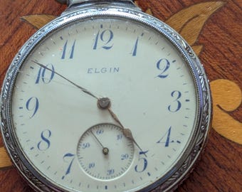 Reloj de bolsillo Elgin de 1910, con caja ornamentada, tamaño 16 y 7 rubíes, funcionando y marcando la hora.