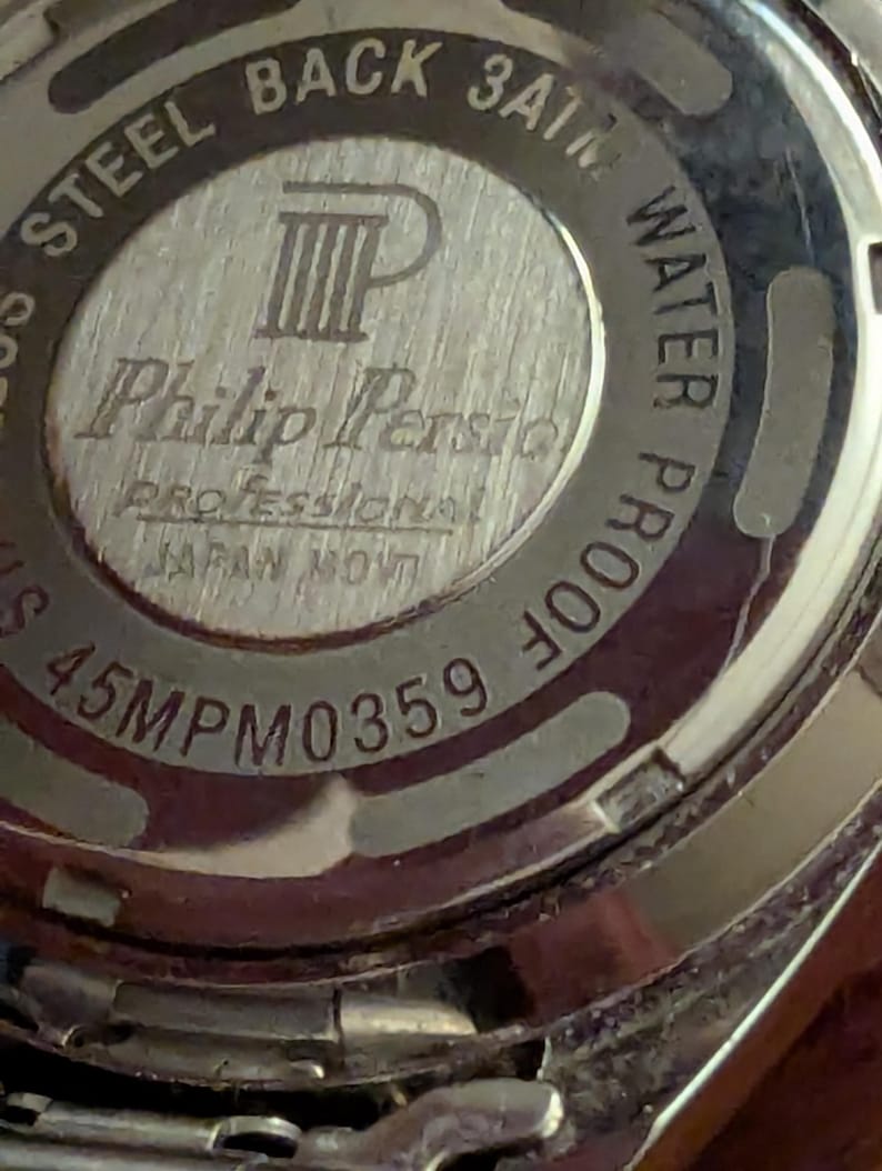 May include: The silver-toned circular case back of a Philip Persio watch features engraved text including STEEL BACK, 3ATM WATER PROOF, PROFESSIONAL, JAPAN MOV'T, and the model number 45MPM0359. A logo with the letters PP is centered on the metal surface.