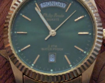 Reloj Phillip Persio con esfera verde, caja de acero inoxidable chapada en oro y brazalete de acero inoxidable, en buen estado de funcionamiento y con buena precisión.