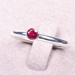 May include: A simple silver band ring with a single round red ruby gemstone.