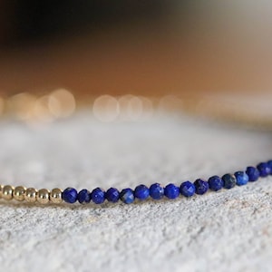 Könnte beinhalten: Ein zartes goldenes Armband mit einer Reihe kleiner, dunkelblauer Lapislazuli-Perlen.