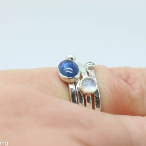 K&ouml;nnte beinhalten: Ein Satz aus drei Silberringen mit Edelsteinen. Der obere Ring hat einen blauen ovalen Edelstein, der mittlere Ring einen klaren runden Edelstein und der untere Ring einen wei&szlig;en ovalen Edelstein.