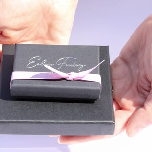 K&ouml;nnte beinhalten: Eine schwarze Geschenkbox mit einem rosa Band und dem Text "Edible Frosty" auf der Oberseite.