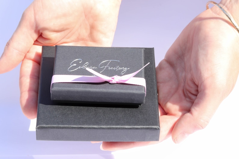 K&ouml;nnte beinhalten: Eine schwarze Geschenkbox mit einem rosa Band und dem Text "Edible Frosty" auf der Oberseite.