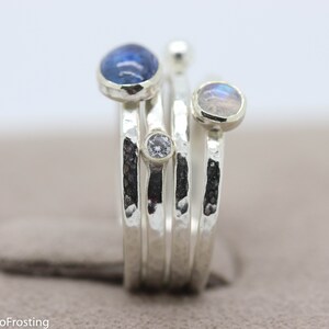 K&ouml;nnte beinhalten: Ein Silberring mit vier Steinen. Der Ring besteht aus mehreren B&auml;ndern mit einer geh&auml;mmerten Textur. Die Steine sind ein blauer Edelstein, ein wei&szlig;er Edelstein und zwei schillernde Mondsteine.
