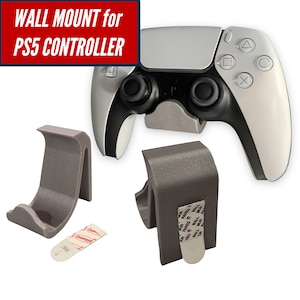 May include: A gray wall mount for a PS5 controller. The mount is designed to hold the controller securely. The image also shows a PS5 controller and a 3M adhesive strip.