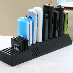 May include: A black plastic organizer with slots for storing various memory cards and USB drives. The organizer has a slot for SD cards, micro SD cards, and a larger slot for USB drives. The organizer is filled with various memory cards and USB drives, including a blue USB drive, a white USB drive, and a black USB drive.