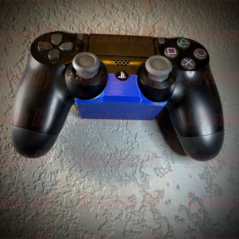May include: A black PlayStation 4 controller with blue and black accents is mounted on a blue stand. The controller has a PlayStation logo on the front.