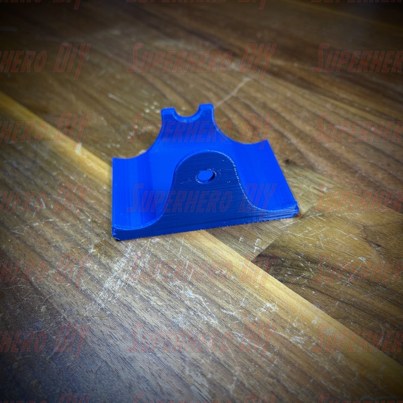 May include: A blue 3D printed plastic wall mount with a hole in the center. The mount is designed to hold a small object, such as a phone or a tablet.