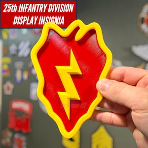 May include: A 3D-printed display insignia of the 25th Infantry Division featuring a shield-shaped red background with a yellow border and a central yellow lightning bolt. The text 25th INFANTRY DIVISION DISPLAY INSIGNIA is visible at the top.