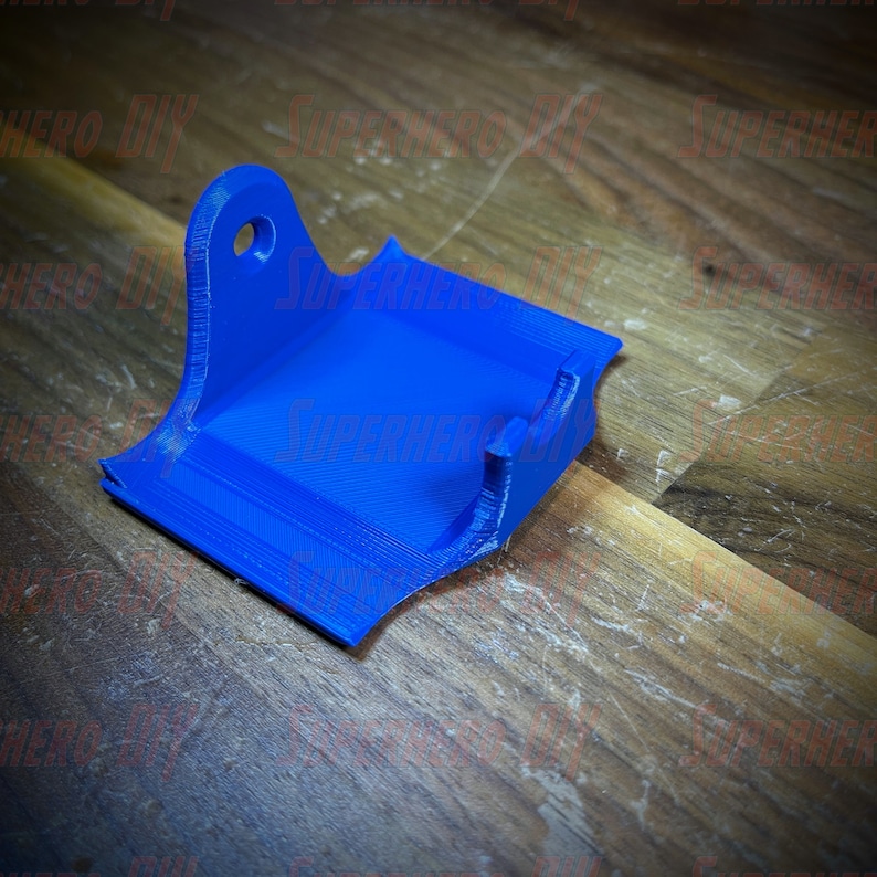 May include: A blue 3D printed wall mount with a hole for mounting. The mount is designed to hold a small object, such as a phone or a tablet.
