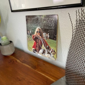 May include: A vintage vinyl record album cover featuring Janis Joplin. The cover art shows Janis Joplin in a red and gold jacket, riding a motorcycle. The album title is "Janis Joplin's Greatest Hits".