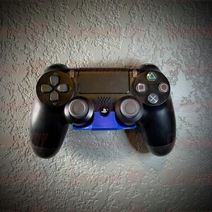 May include: A black PlayStation 4 controller with a blue wall mount. The controller has a textured surface and a PlayStation logo on the front.
