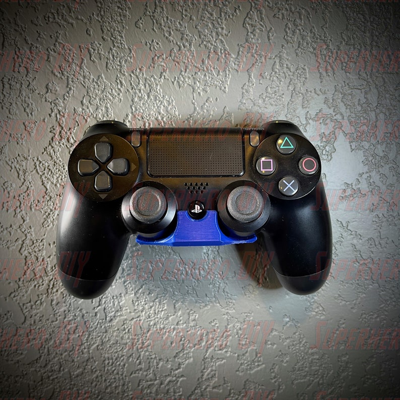 May include: A black PlayStation 4 controller with a blue wall mount. The controller has a textured surface and a PlayStation logo on the front.