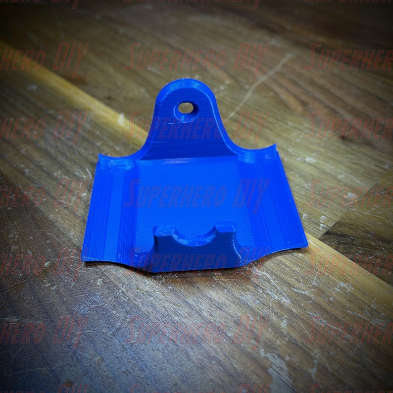 May include: A blue 3D printed wall mount with a slot for a phone or other device. The mount has a hole at the top for hanging.
