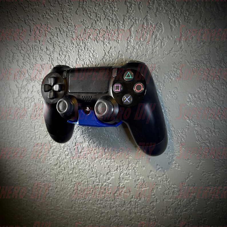 May include: A black PlayStation 4 controller with blue accents is mounted on a wall. The controller has a textured surface and a variety of buttons, including the PlayStation logo, the directional pad, the action buttons, and the share button.