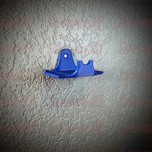 May include: A blue plastic wall mount with a curved design. The mount has a hole in the top for hanging and a small shelf on the bottom.