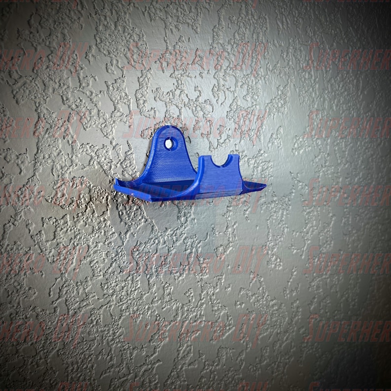 May include: A blue plastic wall mount with a curved design. The mount has a hole in the top for hanging and a small shelf on the bottom.