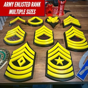 May include: A collection of yellow and black Army enlisted rank insignia, including chevrons and other symbols. The text "ARMY ENLISTED RANK MULTIPLE SIZES" is displayed in a red box. Various sizes and styles are shown, along with miniature castle models.